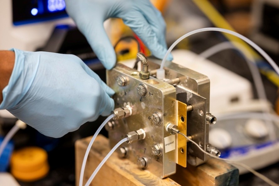 Gloved hands connecting electrolyte lines to an aluminum-air test cell on a lab bench