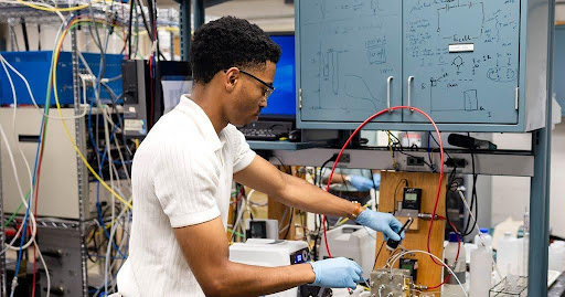 Researcher in a lab coat adjusting instrumentation on a test bench surrounded by cabling